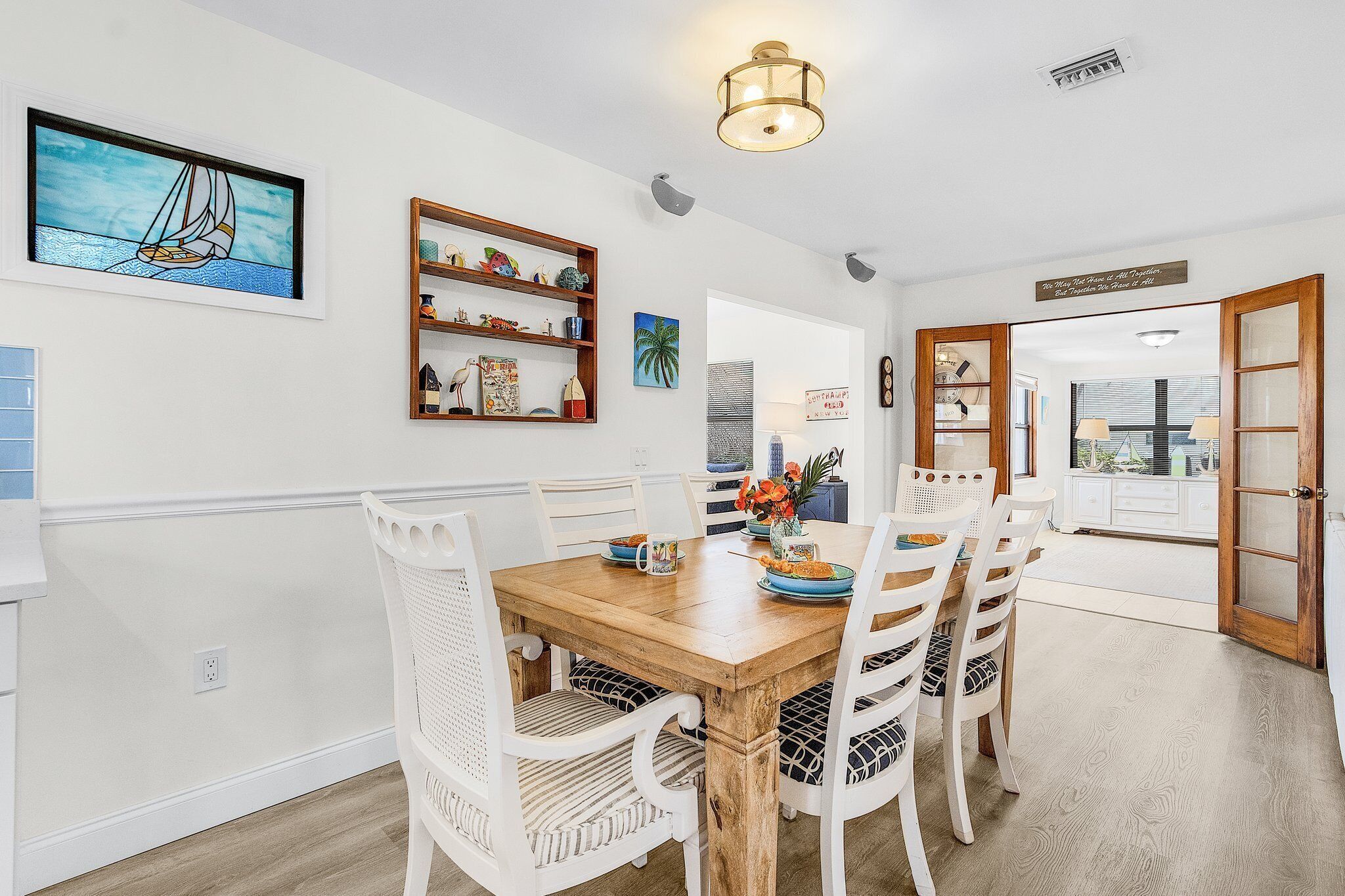 A dining area with a wooden table and white chairs, a wall-mounted shelf with decorative items, and a ceiling light fixture.
