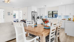 A modern kitchen with white cabinetry, a wooden dining table, and white chairs. - Gulf Access, Heated Pool & Spa, Tiki Hut - Roelens (Fort Myers Beach)
