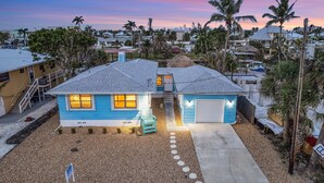 A two-story house with a blue exterior, a front porch, and a driveway leading to a garage. - Gulf Access, Heated Pool & Spa, Tiki Hut - Roelens (Fort Myers Beach)