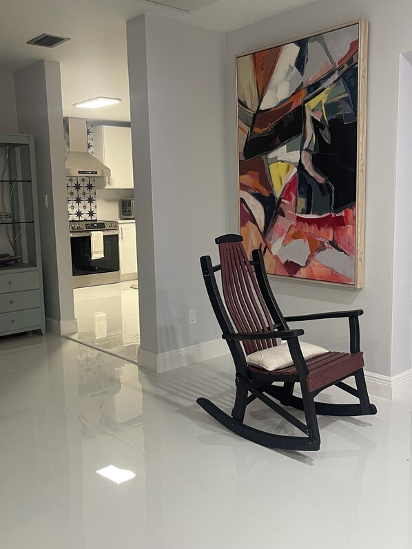 A modern living room with a black rocking chair, a large abstract painting on the wall, and a kitchen in the background. - Great location  (Fort Myers)