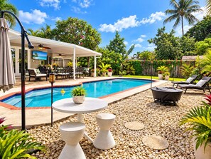 Une piscine avec un patio couvert, des chaises longues et une table agrémentée d’une plante en pot.