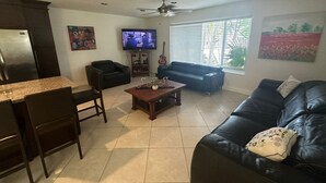 Ein Wohnzimmer mit einem schwarzen Ledersofa, einem Holztisch, einem Fernseher, einem Deckenventilator und einem Fenster mit Jalousien.