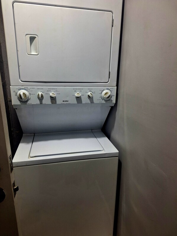 A compact, white, wall-mounted washing machine with multiple control knobs for temperature and cycle settings.