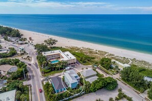 Vista aérea de un hotel frente al mar con piscina, acceso a la playa y una carretera que lleva a la propiedad.