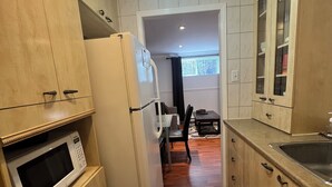 Ett kompakt kök med träskåp, en inbyggd mikrovågsugn, ett kylskåp och en diskho.