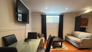 Ett modernt vardagsrum med ett matbord i glas, svarta stolar, en soffa och en platt-TV som är monterad på väggen.