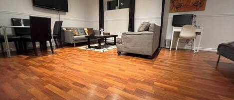 A modern living room with hardwood flooring, a grey sofa, a coffee table, and a flat-screen TV mounted on the wall.