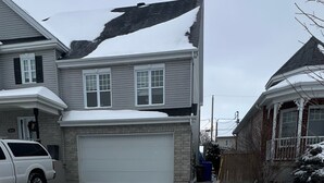 Ett bostadshus med ett garage, en uppfart som delvis är täckt av snö och en vit pickup-truck parkerad på vänster sida.