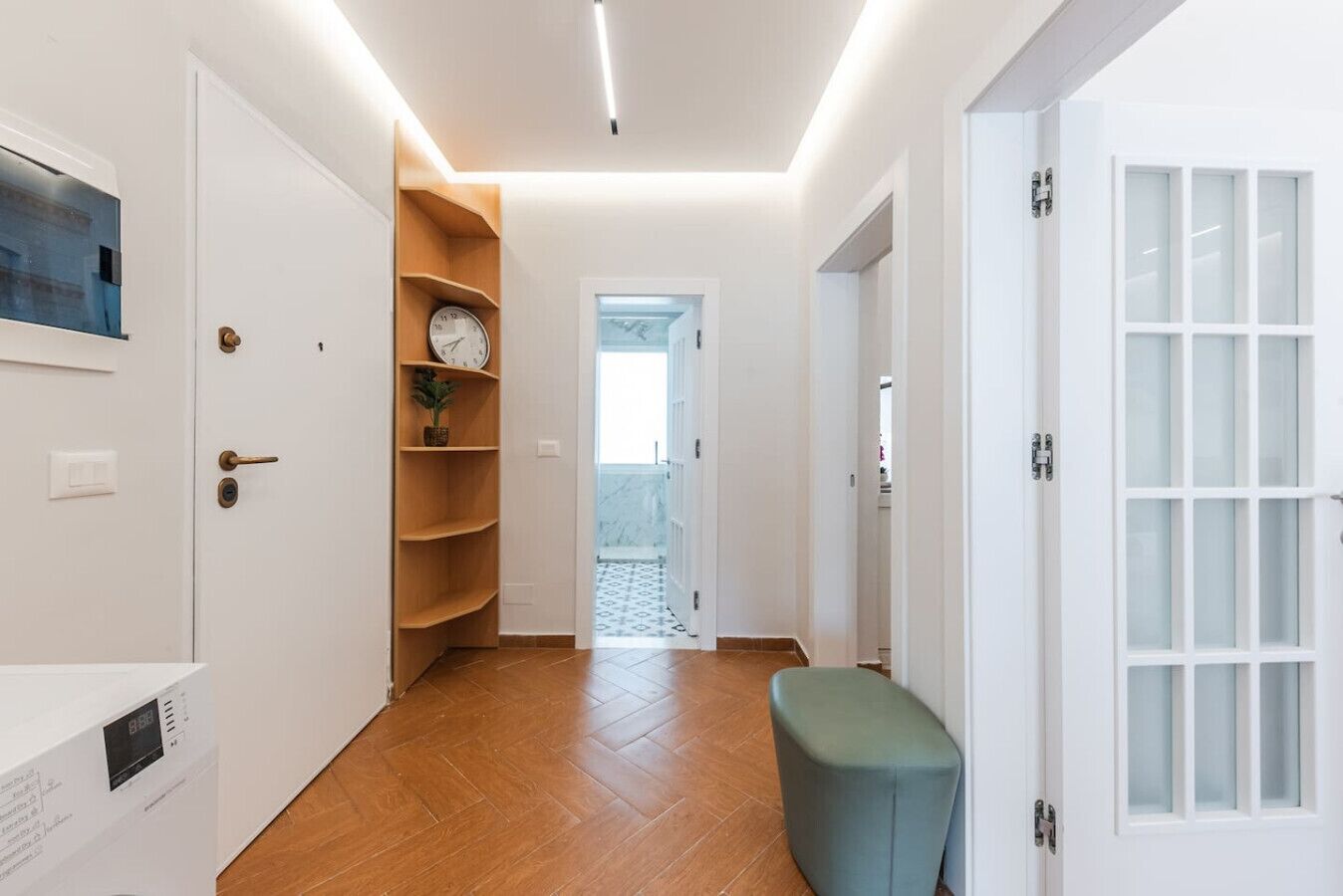 Un pasillo con piso de madera, un reloj en un estante y un banco.
