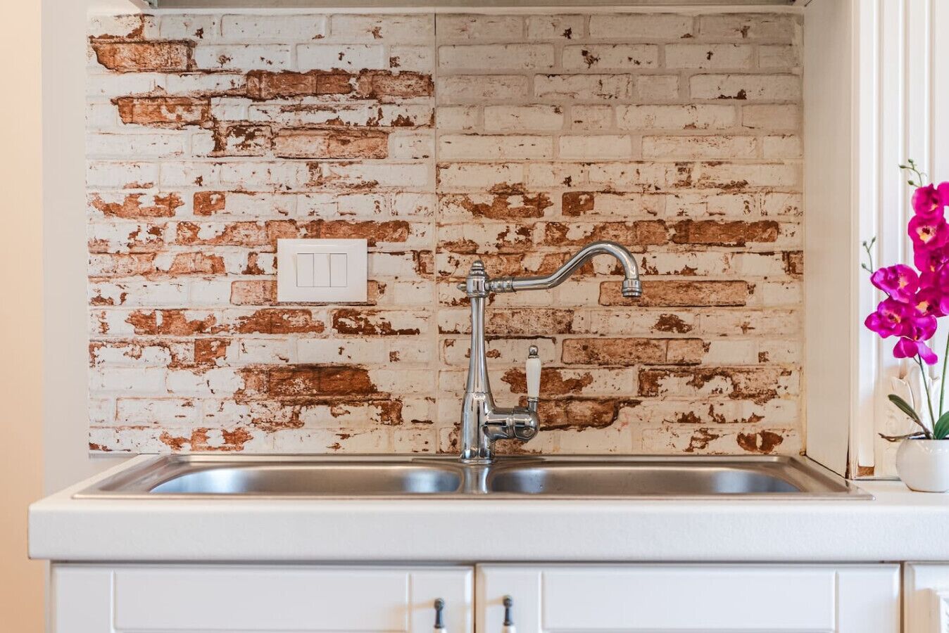A kitchen with a white brick backsplash, a stainless steel sink, and a white cabinet below.