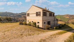 A stone house with a sloped roof, a gravel driveway, and a rural landscape in the background.