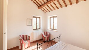 A bedroom with a bed, two windows, a radiator, and two striped chairs.