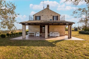 A two-story stone house with a tiled roof, a covered patio with seating, and a view of the surrounding landscape. - Villa Francesca - Fermo, wonderful villa in the Marche hills (Petritoli)