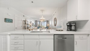 A modern kitchen with white cabinetry, a dishwasher, and a coffee maker. - Waterscape B105 ~ 2BR Ground Floor ~ Gulf Views! (Fort Walton Beach)