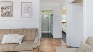 A modern living room with a sofa, a glass-enclosed shower, and a bed in the background. - Cozy Pet Friendly Beach House (Kingscliff)