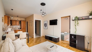 A modern living room with a sofa, a coffee table, a TV, and a kitchen in the background.