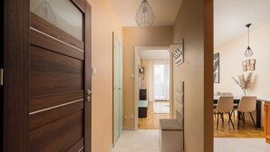 A hallway with a wooden door, a dining area with a table and chairs, and a hanging light fixture.