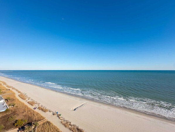 A beach with a clear sky, a sandy shore, and a wooden jetty.