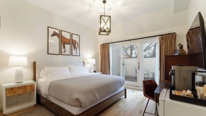 A bedroom with a large bed, bedside tables with lamps, a TV, and a sliding glass door to the outside. - The Townsman: Secretariat Room (Charlottesville)