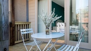 A balcony with a round table, two white chairs, and a vase with white flowers. - The Townsman: Meriwether Room (Charlottesville)