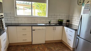 Una cocina con armarios blancos, lavavajillas, fregadero, estufa y refrigerador.