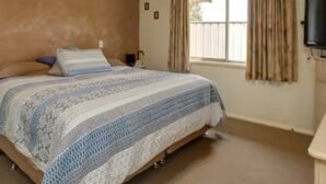 Un dormitorio con una cama, ventilador de techo, ventana con cortinas y televisor montado en la pared.
