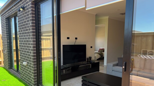 A modern living room with a flat-screen TV, a sofa, and a coffee table. - 4-bedroom Family home /WFH vacation living in Tarneit, West Melbourne (Tarneit)
