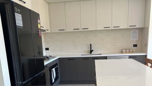 A modern kitchen with a black refrigerator, a built-in oven, and a white countertop. - 4-bedroom Family home /WFH vacation living in Tarneit, West Melbourne (Tarneit)