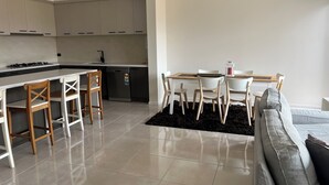 A modern kitchen with a central island, a dining area with a table and chairs, and a living area with a sofa and a rug. - 4-bedroom Family home /WFH vacation living in Tarneit, West Melbourne (Tarneit)