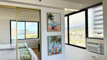 A bedroom with a bed, a large window with a city view, and two wall-mounted pictures.