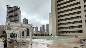 A rooftop pool area with a white pergola, lounge chairs, and a caution sign for slippery surfaces when wet. - Waikiki Studio with Stunning Views! (Honolulu)