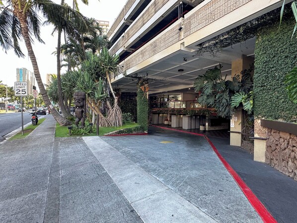 A hotel entrance with a covered walkway, palm trees, and a speed limit sign of 25.