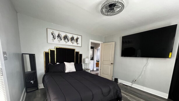 Un dormitorio moderno con una cama grande, un televisor de pantalla plana, un ventilador de techo y una puerta que da a otra habitación.
