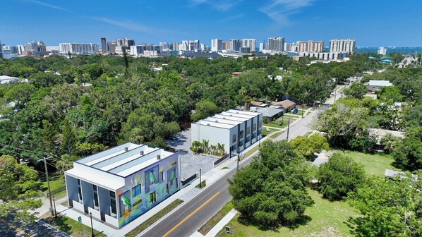 A modern building with a flat roof and a colorful mural on one side, surrounded by lush greenery and a clear blue sky. - Luxury Park-View Townhome | EV Charger | Walk to Downtown Sarasota /Sleeps 4 (Sarasota)