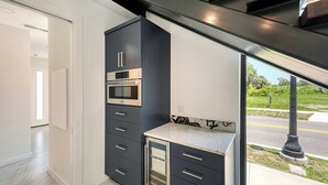A modern kitchen with built-in appliances, a marble countertop, and a view of the street.