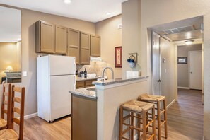 A kitchen with a refrigerator, stove, and wooden bar stools.