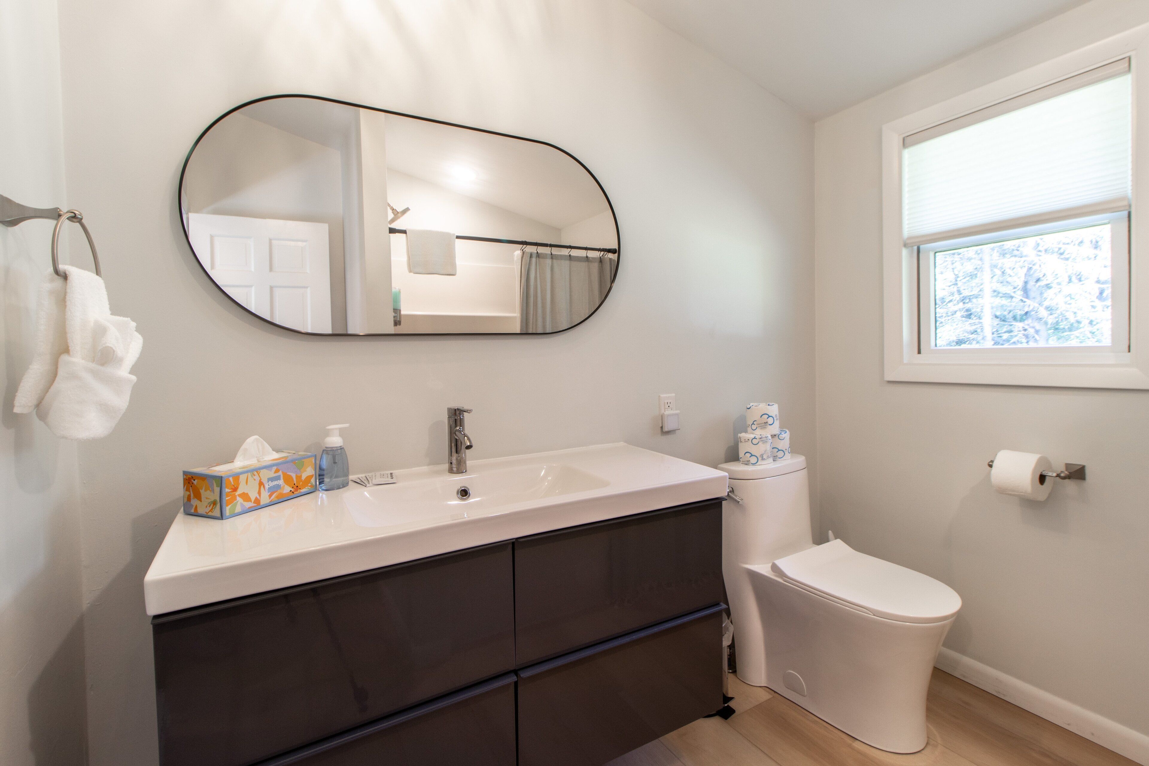 A bathroom with a white sink, dark cabinets, a toilet, and a large mirror.