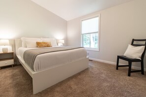 Ein Schlafzimmer mit Bett, Nachttischen, einem Sessel und einem großen Fenster.