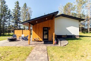 Eine Holzhütte mit überdachter Veranda, Sitzgelegenheit im Freien und einem Feuerkorb.