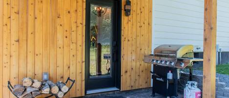 Fachada de madera con una puerta negra, una parrilla y un banco con leña.