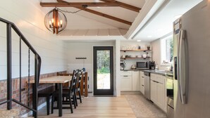 Una cocina moderna con armarios blancos, un refrigerador de acero inoxidable y un comedor con mesa y sillas de madera.