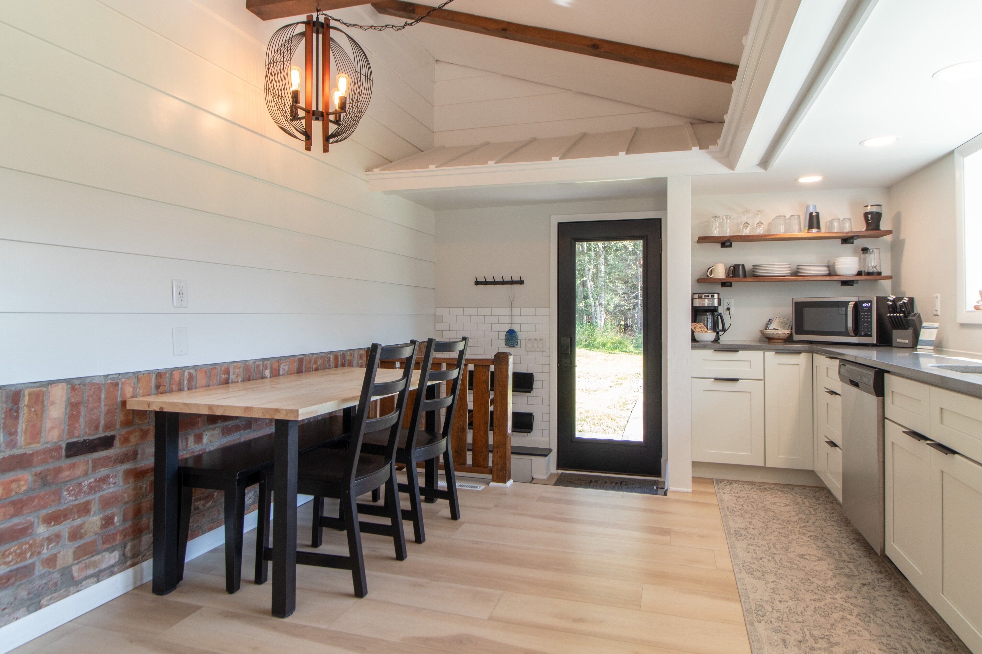 A modern kitchen with a wooden dining table and chairs, white cabinetry, and a brick accent wall.