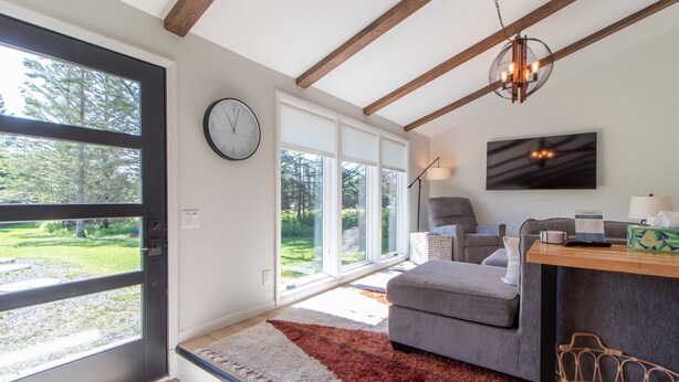 Una sala de estar moderna con un sofá gris, una mesa de centro de madera y un amplio ventanal con persianas.
