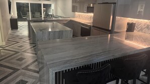 A modern kitchen with a marble countertop, stainless steel appliances, and a herringbone-patterned floor.