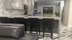 A modern kitchen with a central island, black upholstered chairs, and a black leather sofa.