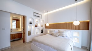 A modern bedroom with a large bed, built-in shelving with decorative items, a wooden headboard, and pendant lighting. - Villa Ratu Canggu (Canggu)