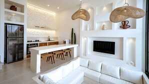 A modern kitchen with a central island, a dining area, and a living room with a sofa and TV. - Villa Ratu Canggu (Canggu)