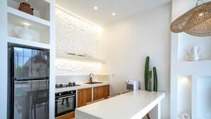 A modern kitchen with a large island, stainless steel appliances, wooden cabinets, and a stone backsplash. - Villa Ratu Canggu (Canggu)