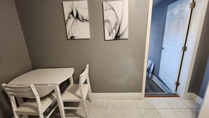 A room with a white table and chairs, two abstract paintings on the wall, and a door leading to a hallway.