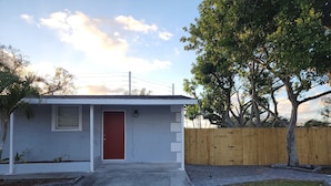 A small single-story house with a red door, a small window, and a wooden fence.